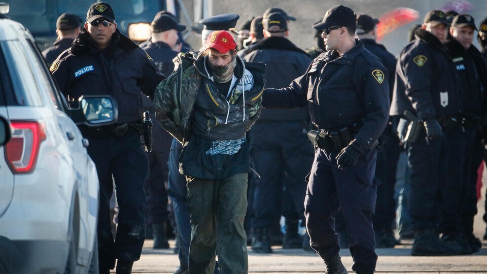 Des policiers accompagnent un homme menotté.