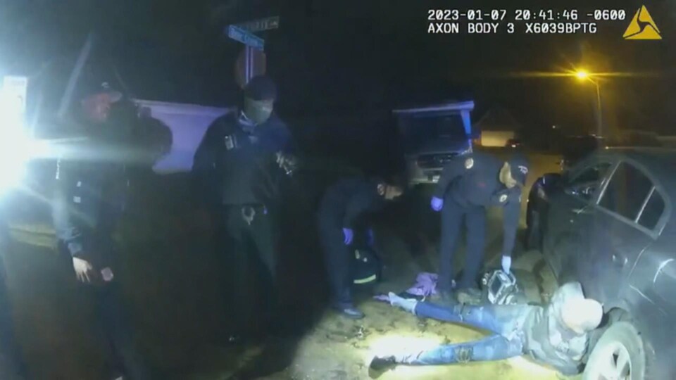 Tyre Nichols est étendu et appuyé contre une voiture tandis que des policiers le regardent.
