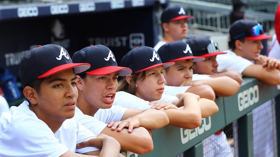 Des jeunes joueurs de baseball autochtones alignés derrière une clôture de métal.