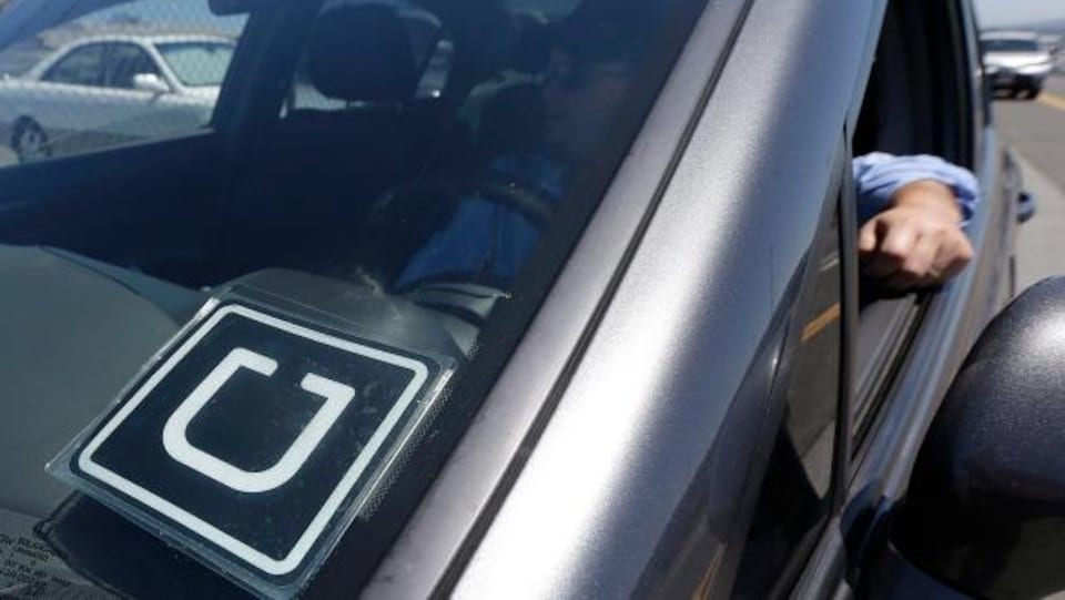 Une voiture Uber avec le logo et quelqu'un assis au volant. On voit son bras qui sort de la fenêtre de la voiture, qui est baissée.