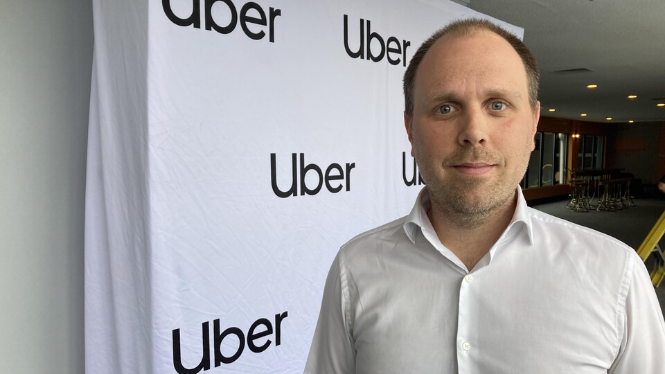 Un homme pose devant une affiche d'Uber.