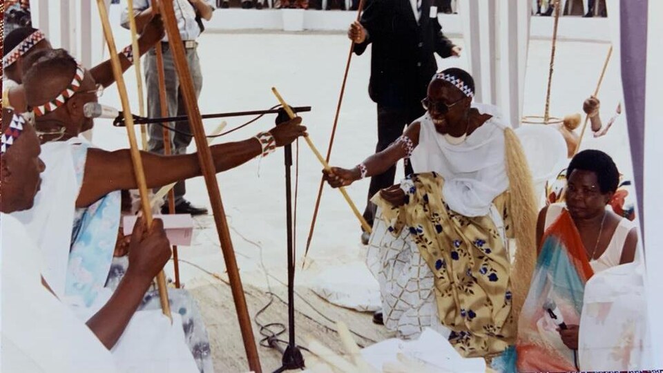 Un homme en costume traditionnel reçoit un sceptre lors d'une cérémonie en Afrique.