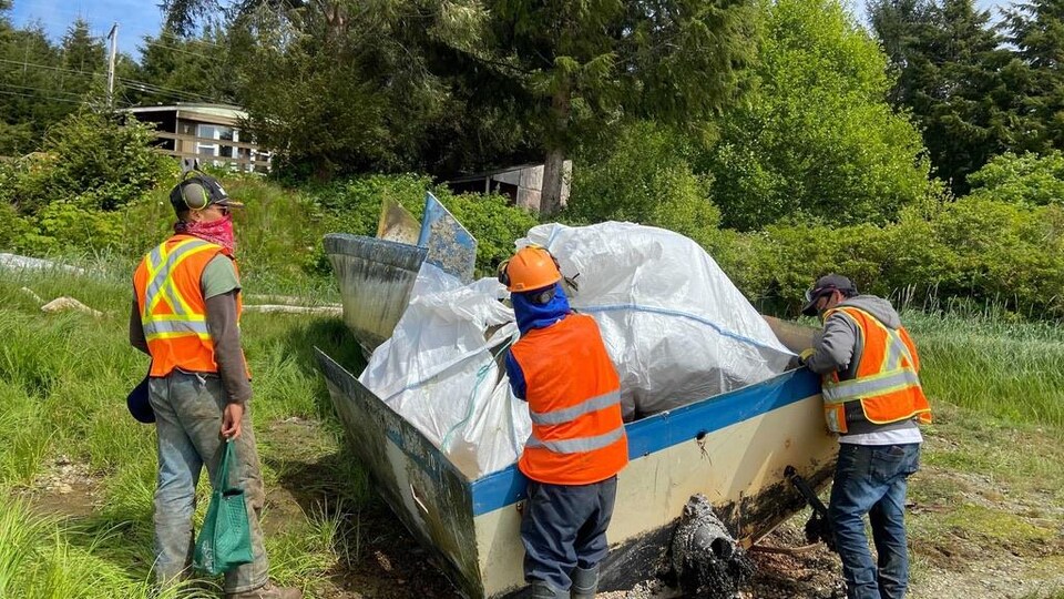 Trois hommes s'affairent autour d'une épave.