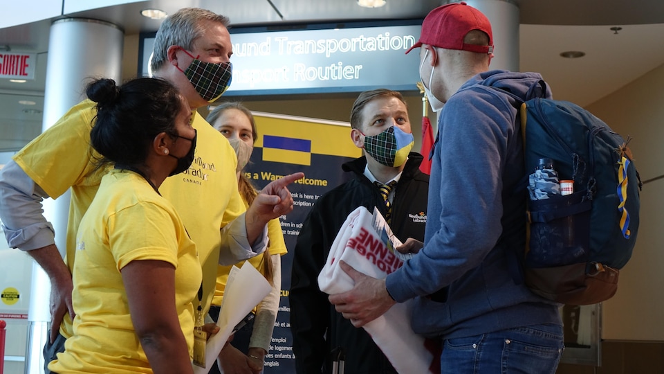 A man with a backpack at an airport talking to several people.