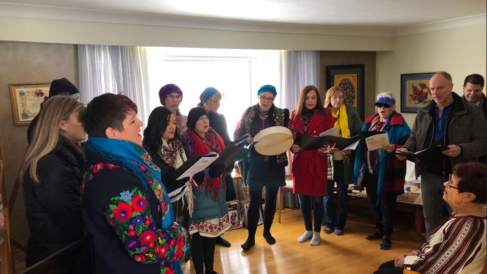 Une chorale entonne des chansons dans le salon d'une maison. 