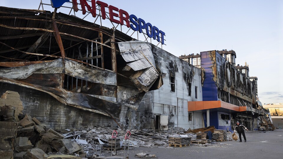 Un homme transporte des cartons d'un centre commercial détruit à Boutcha, en Ukraine.