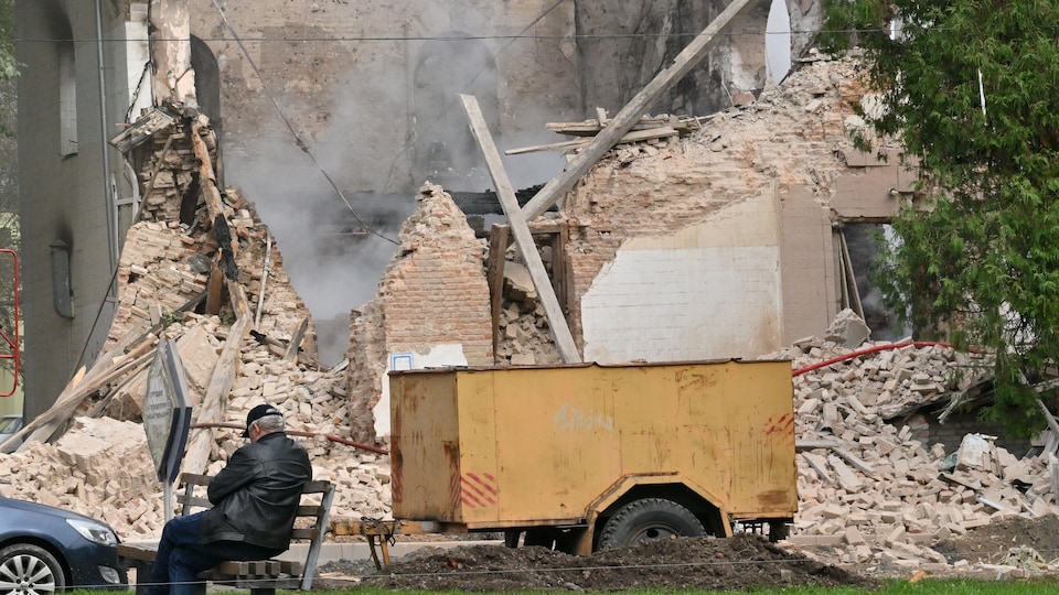 Un homme assis devant un immeuble détruit par des bombardements.