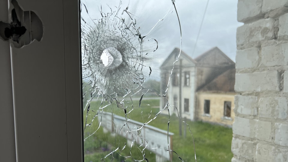 Une vitre percée d'une balle à travers laquelle on voit un édifice incendié sans toit.