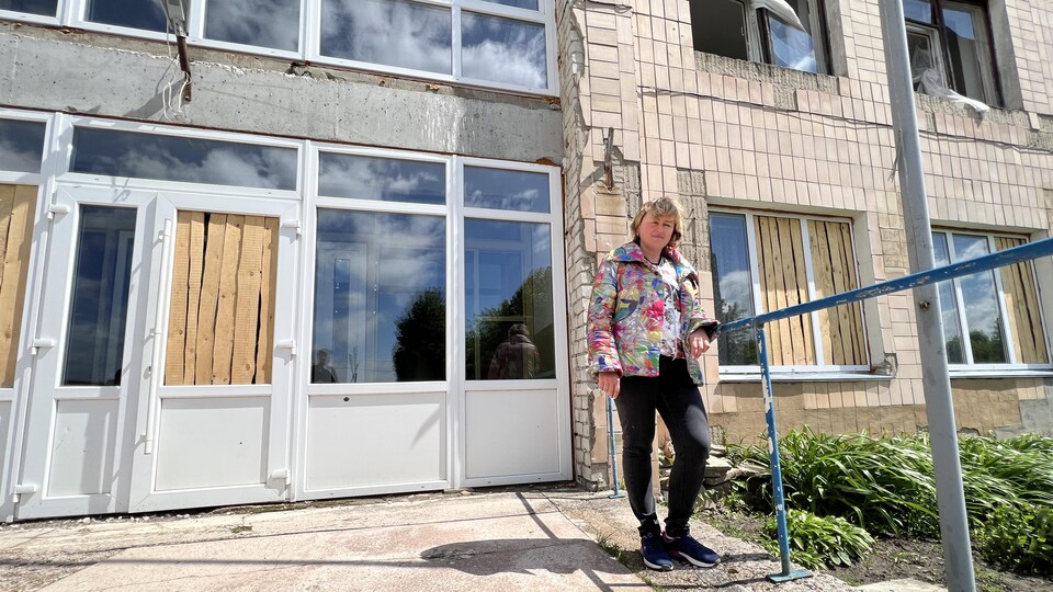 Valentina Kouznetsova est accoudée à une rampe devant un édifice aux vitres cassées ou placardées.