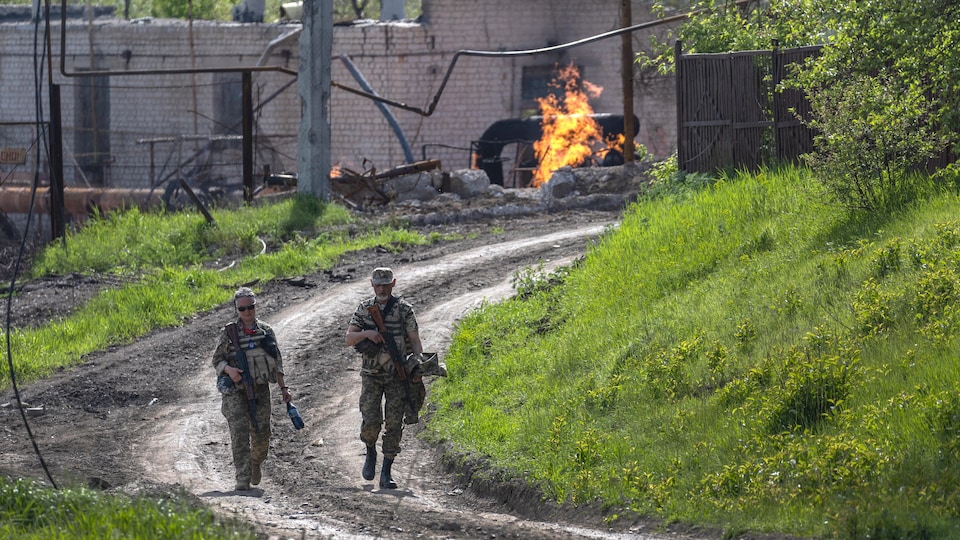 Des soldats marchent sur un chemin sur le côté duquel des flammes jaillissent.