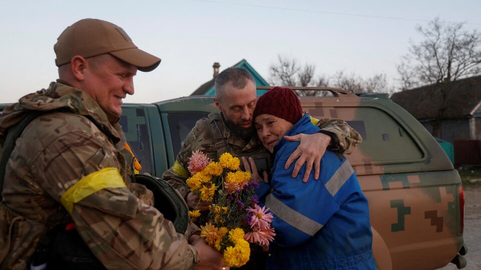 Une femme dans les bras d'un soldat avec un bouquet de fleurs.
