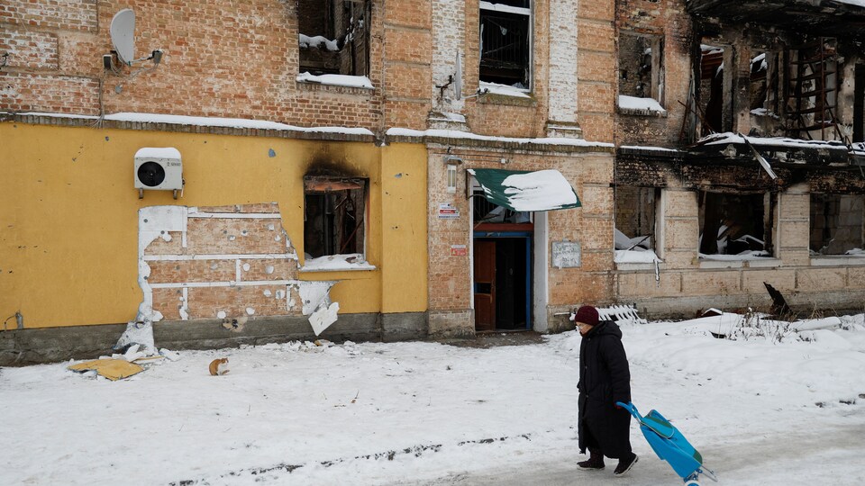 Une Ukrainienne marche dans la neige devant un immeuble délabré.