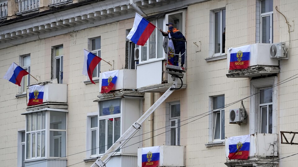 Un homme agite un drapeau russe à la fenêtre d'un immeuble.
