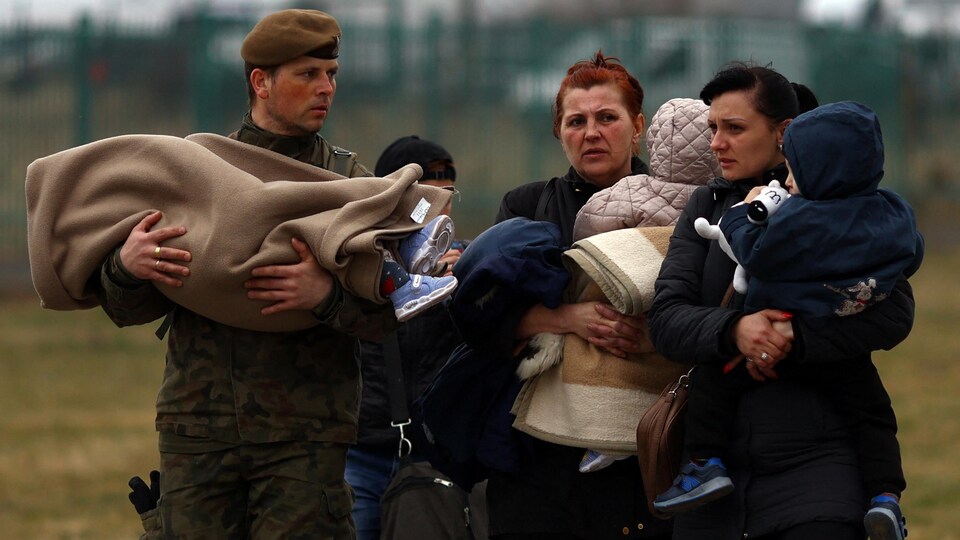 Des femmes et des enfants traversent la frontière polonaise et sont aidés d'un soldat du pays.