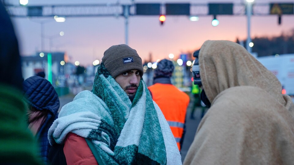 Des personnes emmitouflées dans des couvertures attendent au petit matin près d'un poste frontalier.