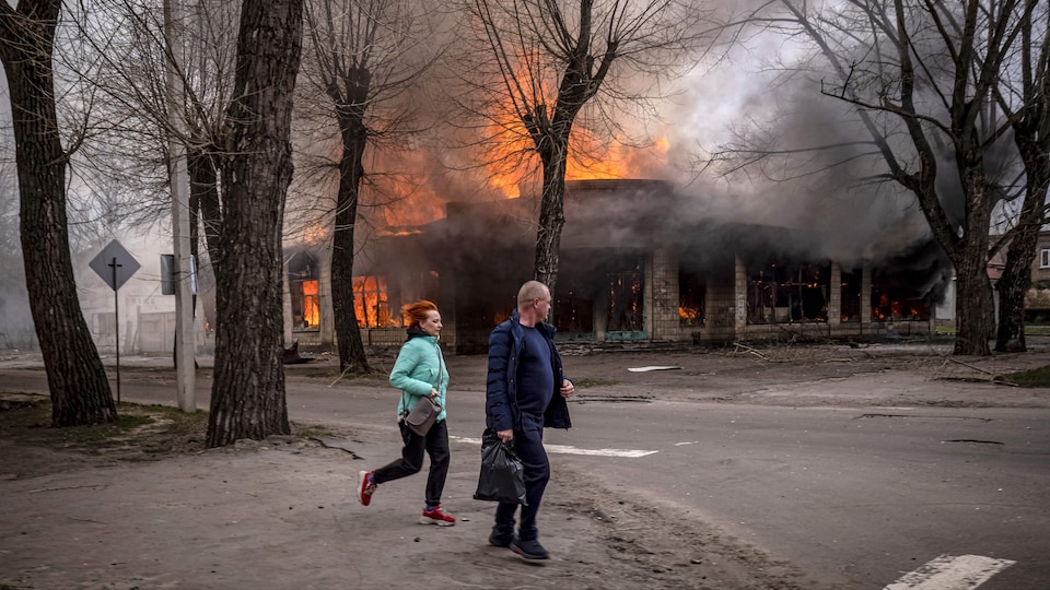 Un homme et une femme fuient près d'un bâtiment en feu.