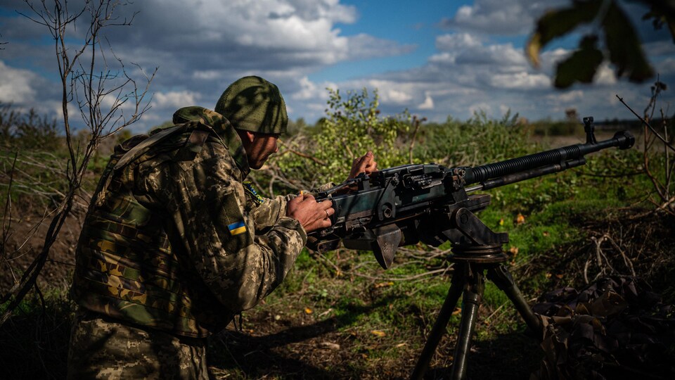 A Ukrainian soldier stands behind a machine gun.