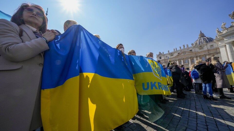 Des pèlerins tiennent un drapeau ukrainien sur la place Saint-Pierre de Rome en attendant la prière du pape.