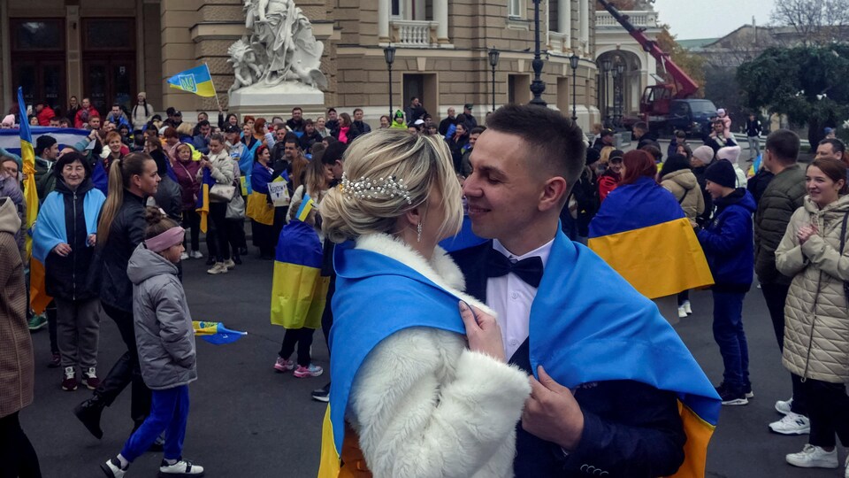 Un homme et une femme s'embrassent avec, autour de leurs épaules, un drapeau ukrainien.