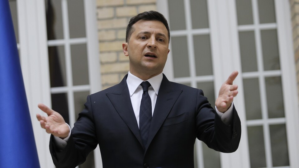 Un homme en conférence de presse à l'extérieur, devant la façade d'un immeuble.