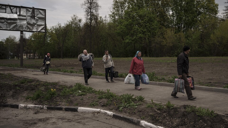 Ukrainians holding bags with their belongings are walking in line. 