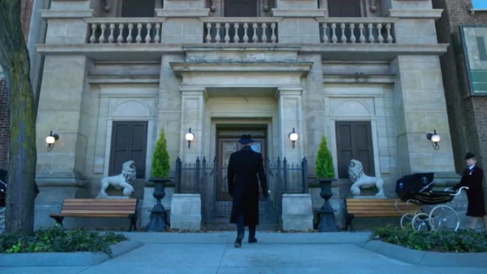 Un homme, vu de dos, marche vers un grand bâtiment d'époque.