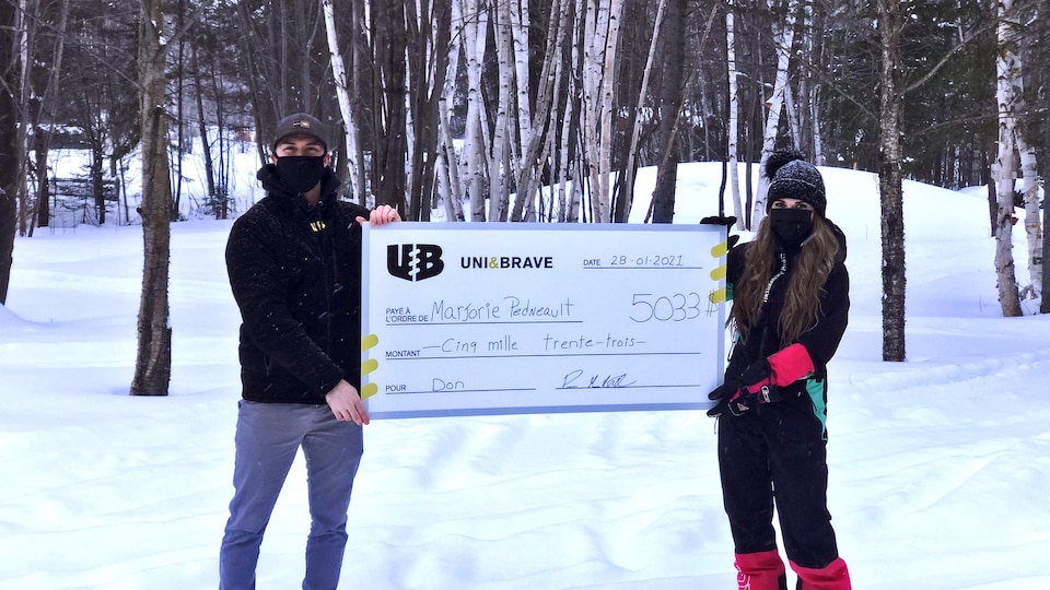 Un homme et une femme masqués tiennent un gros chèque dans une forêt l'hiver.