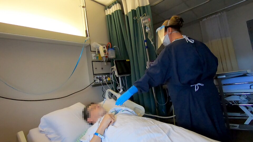 Une infirmière vêtue d'équipements de protection individuelle prend la température d'un patient atteint de la COVID-19 à l'aide d'un thermomètre.