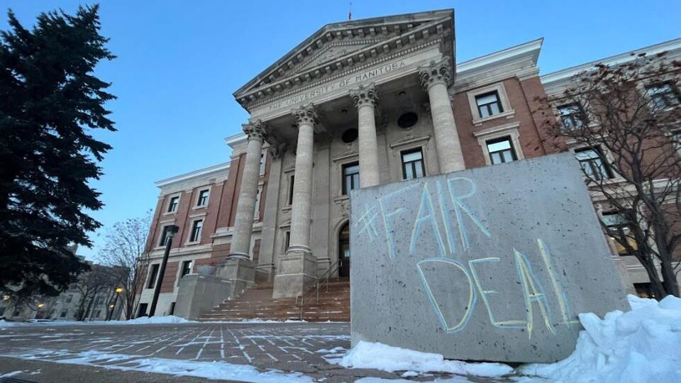 Sur un bloc de béton devant un bâtiment de l’Université du Manitoba, il est écrit à la craie « Fair Deal ».
