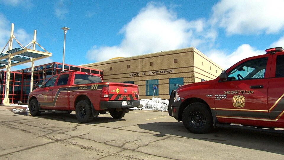 Deux camionnettes rouges des pompiers de Moncton sont immobilisées devant un bâtiment de brique jaune sur lequel les mots « Sciences de l'environnement » sont écrits.