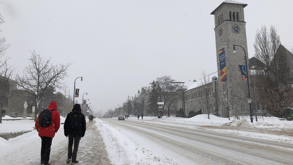 Deux étudiants marchent sur le trottoir enneigé du campus.