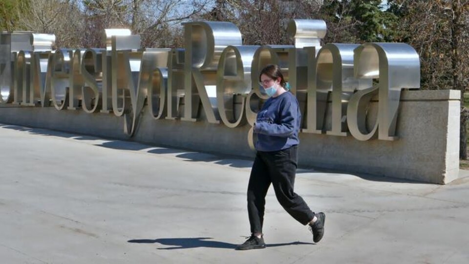 Une étudiante marche devant les lettres géantes en métal sur le campus, qui indiquent le nom de l'Université de Regina.