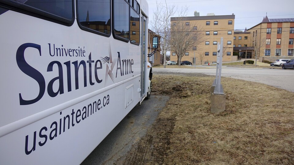 Un autobus marqué du logo de l'Université, près de l'édifice Bernardin-J-Comeau de l'Université Sainte-Anne.