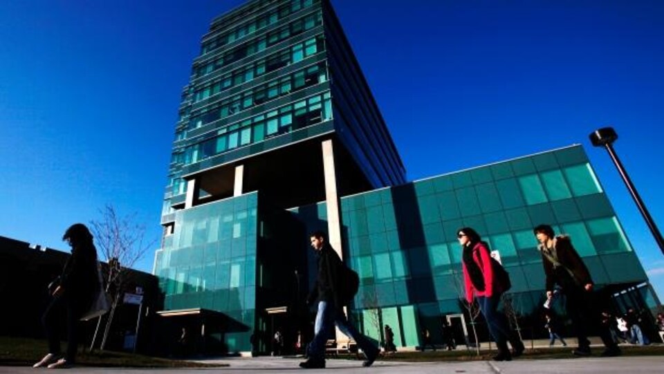 Des étudiants marchent devant un grand édifice en verre de l'université.