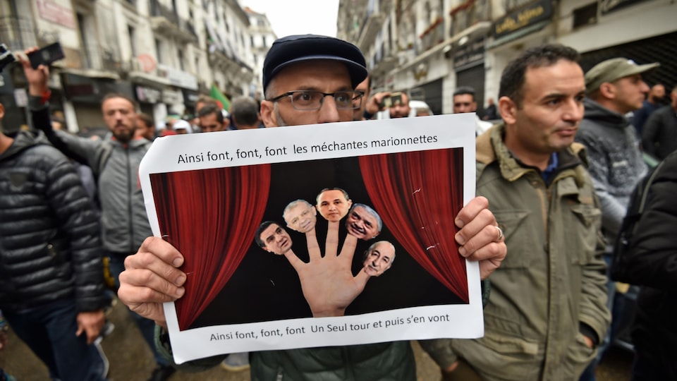 Un manifestant algérien brandit une affiche sur laquelle sont représentés, sur les doigts d'une seule main, les cinq candidats à la présidentielle accusés d'être à la solde du pouvoir en place.
