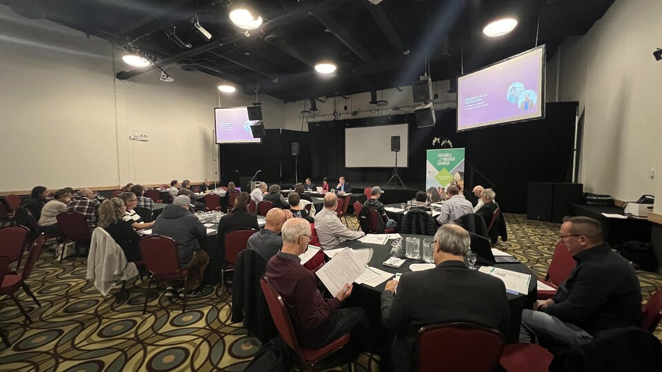 Des gens assis à des tables dans une grande salle de conférence. 
