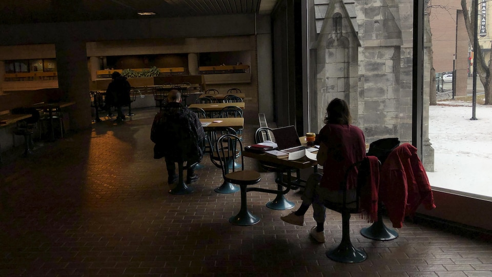 Des gens assis à des tables dans un local vitré.