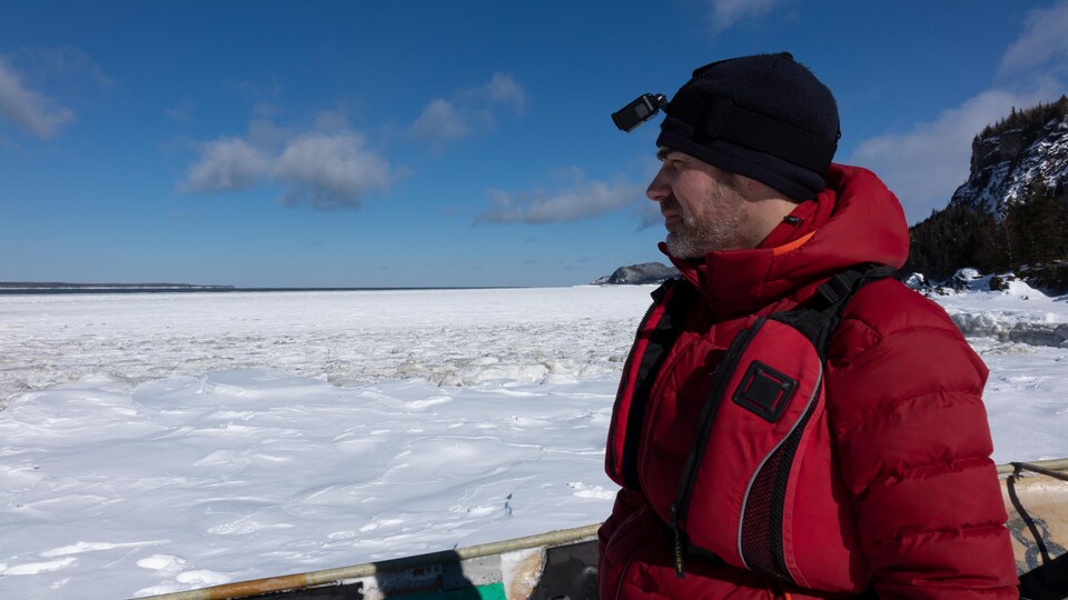 Un homme portant une tuque et un manteau regarde au loin assis dans le canot sur la glace.