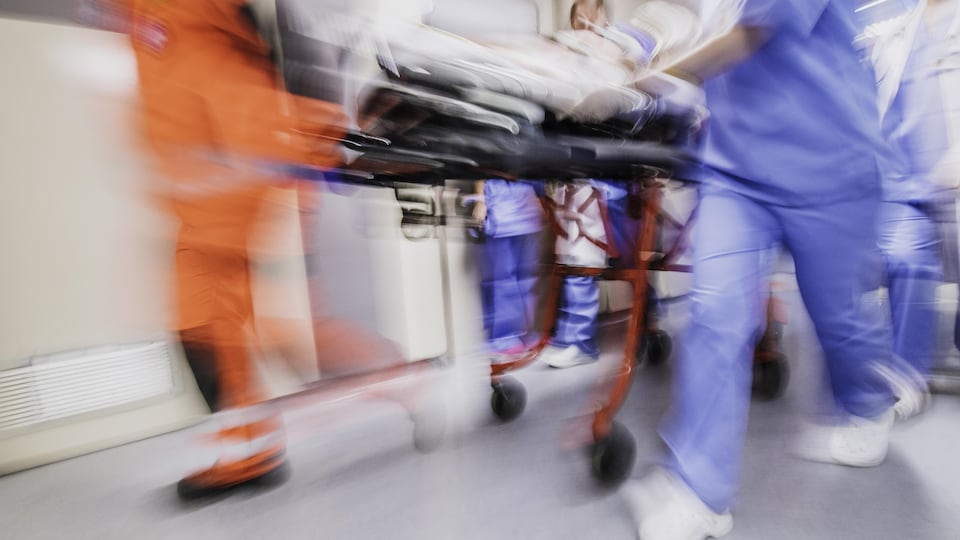 Photo d'infirmiers en mouvement poussant une civière dans un couloir.