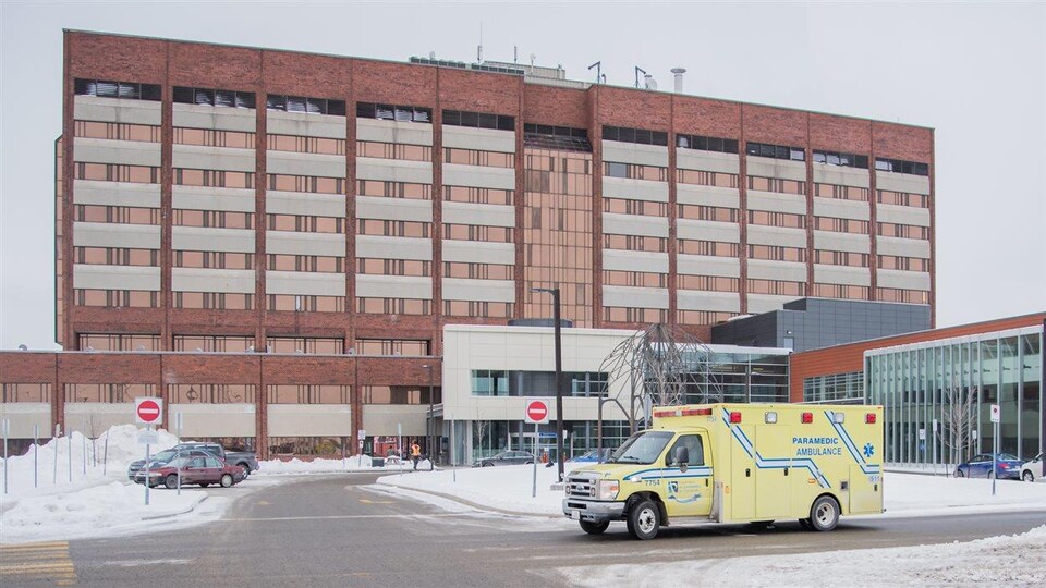 Un véhicule des paramédics circule sur une route enneigée devant un hôpital.