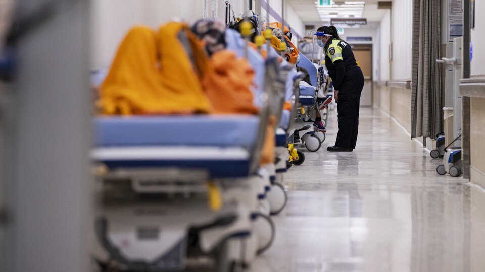Une ambulancière parle à un patient sur une civière dans le corridor de l'urgence.