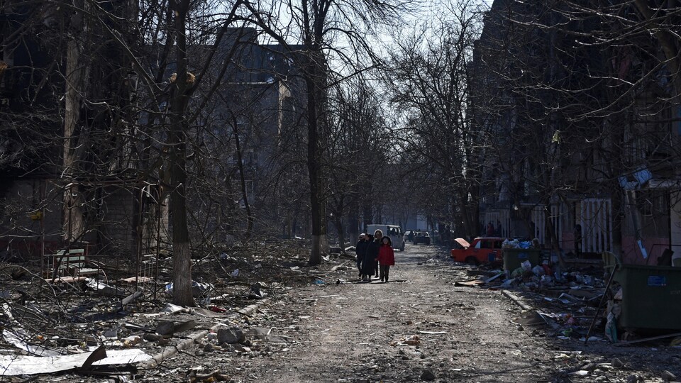 Des gens marchent dans une rue bordée de bâtiments détruits. 
