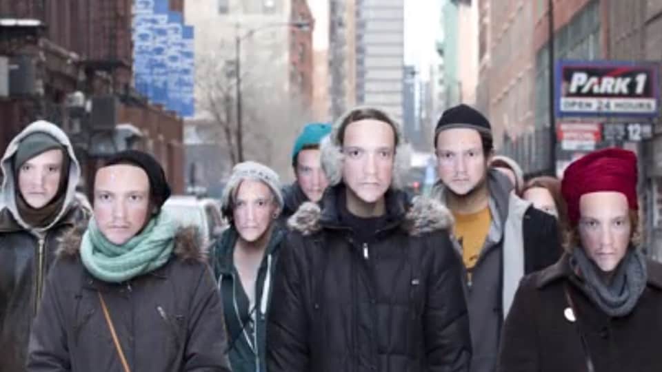 Un groupe de personnes marche dans la rue en portant tous le même masque.