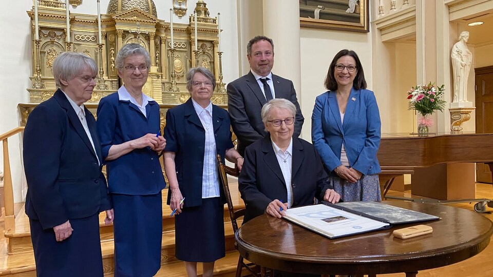 Une soeur signe un document officiel en présence notamment du maire de Trois-Rivières.