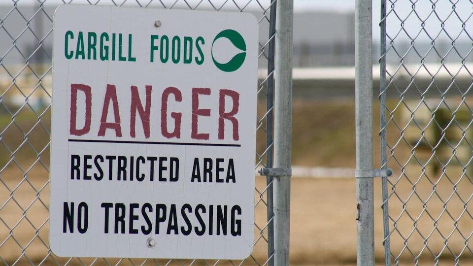 Gros plan sur une affiche mise sur une barrière de l'usine indiquant en anglait: Cargill Foods. Danger. Restricted area. No trespassing.