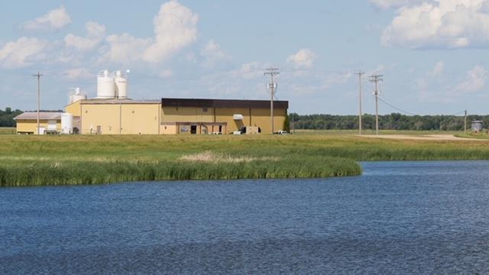 Une usine jaune dans un endroit rural, avec un cours d'eau en avant-plan.
