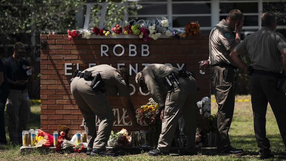 Two men, leaning over, light a candle in front of a memorial erected in honor of the victims of the Uvalde massacre, in the elementary school where it happened.
