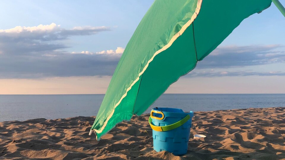 Un seau à sable sous un parasol, sur une plage.