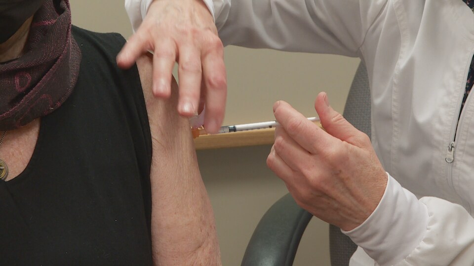 Une infirmière injecte le vaccin dans son épaule.