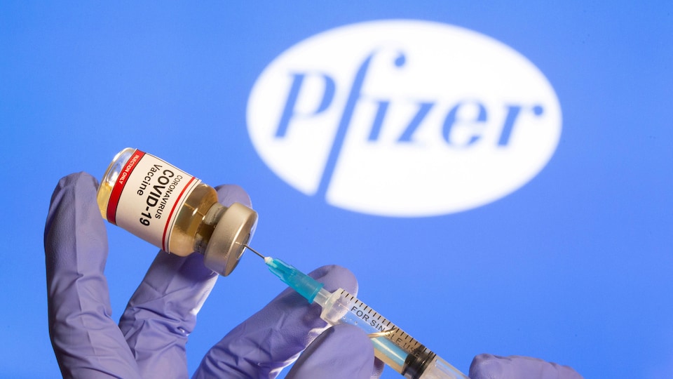 Une seringue est trempée dans une petite bouteille sur laquelle est inscrit le nom d'un vaccin contre la COVID-19, devant un logo de Pfizer.